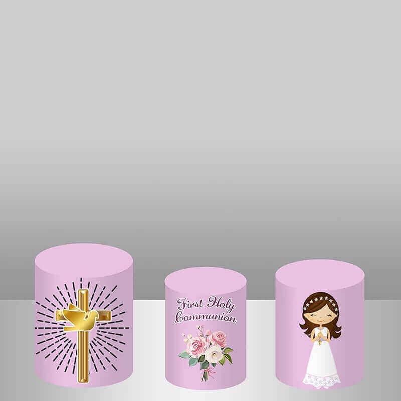 Three coordinating cylinder covers: one with a golden cross, one with 'First Holy Communion' text, and one with an illustration of the girl holding a cross, all matching the floral backdrop.
