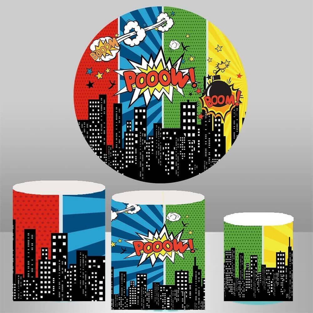 A superhero-themed party backdrop displaying a colorful cityscape with comic book action words like 'POW!' and 'BOOM!', accompanied by three cylinder covers with matching superhero action designs, ideal for children's superhero parties and comic book events.