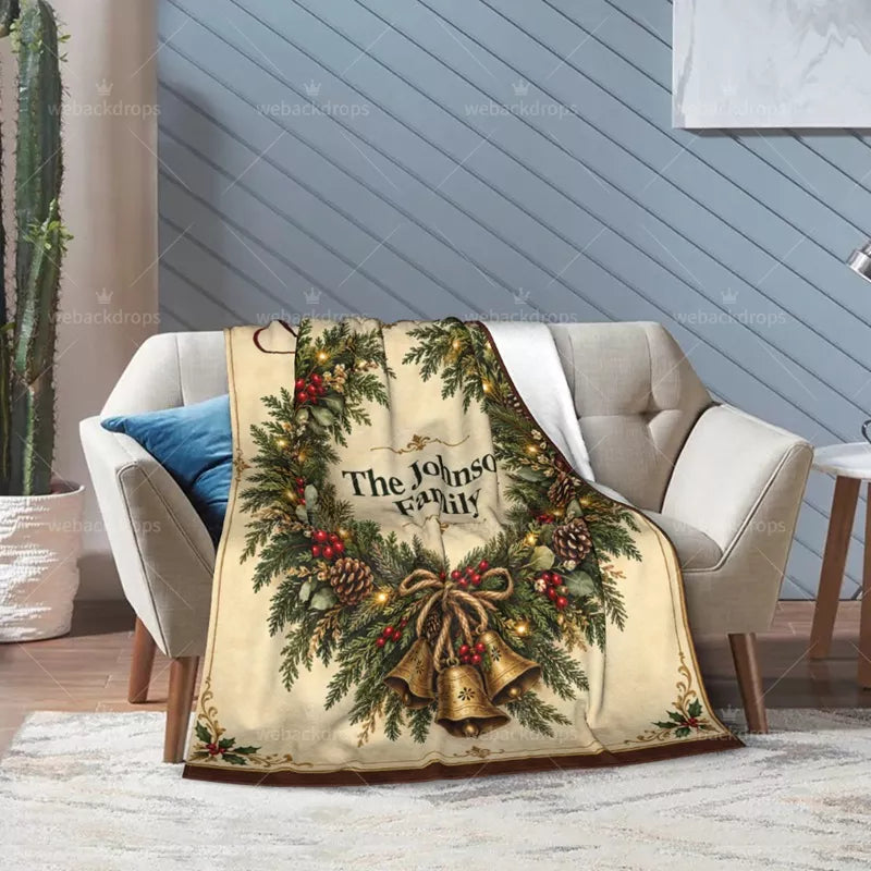 Personalized cedar wreath Christmas blanket draped over a light armchair, showing pinecones, red berries, golden bells, and a white reverse side.