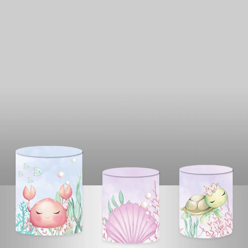 Set of three cylinder covers with ocean-themed illustrations, including a smiling crab, a pink seashell, and a green turtle with a floral crown.