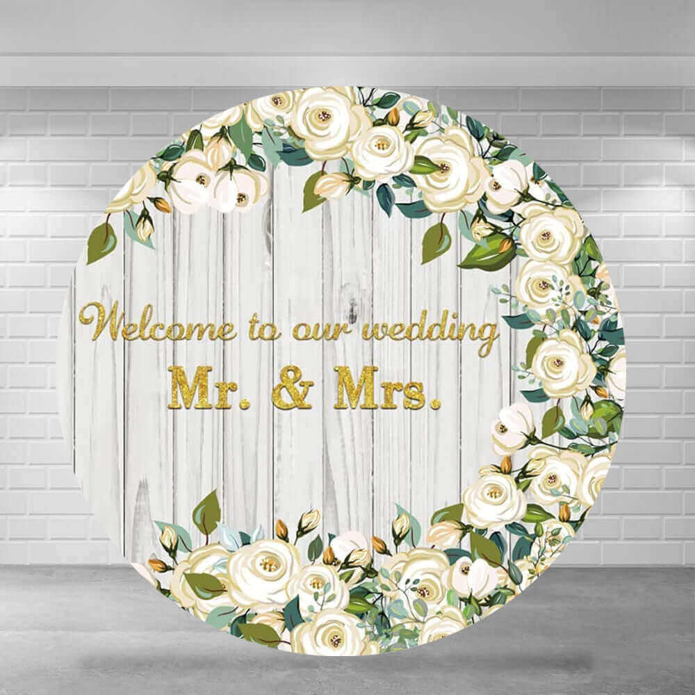 Round wedding backdrop featuring "Welcome to our wedding Mr. & Mrs." in gold letters, surrounded by white roses and greenery on a wooden background, perfect for wedding celebrations.