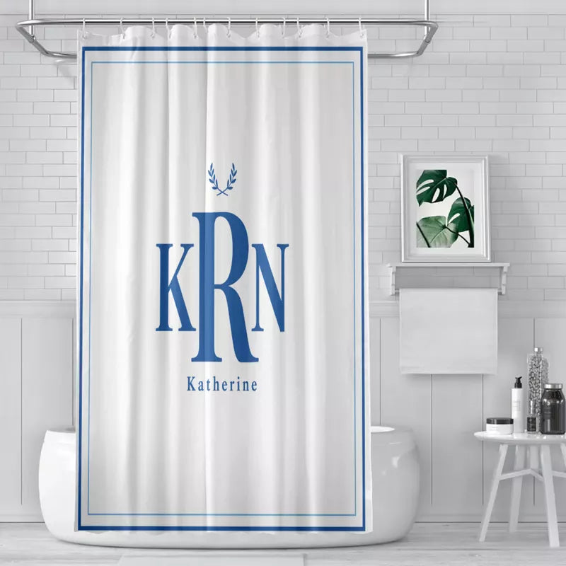 White shower curtain with an elegant blue double border, large KRN monogram, laurel design, and Katherine name hanging over a bathtub in a bright tiled bathroom.