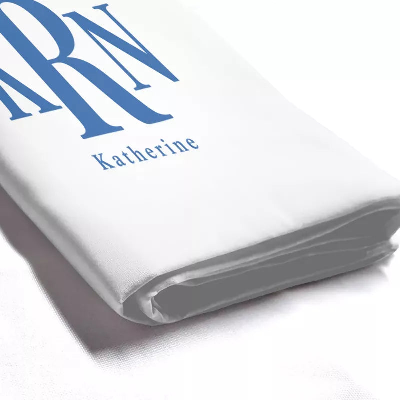 Close-up of folded white shower curtain fabric featuring blue KRN monogram initials and the name Katherine printed beneath.