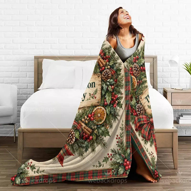 Woman wrapped in a personalized farmhouse Christmas blanket featuring evergreen branches, pinecones, dried orange slices, and a red and green plaid border.