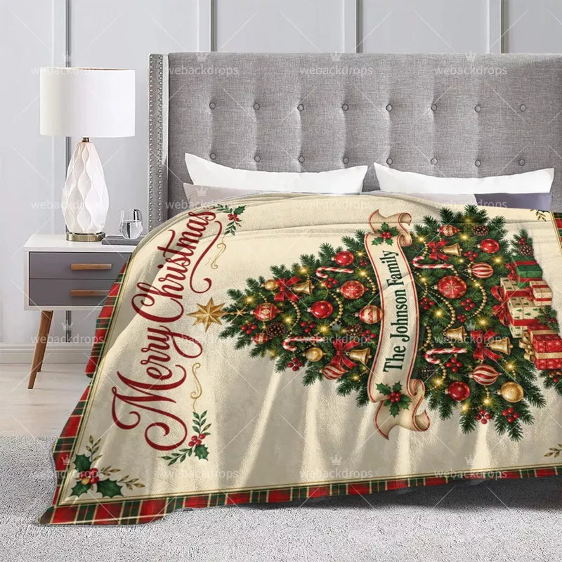 Custom family Christmas blanket displayed on a bed with Merry Christmas text, festive tree ornaments and personalized name.