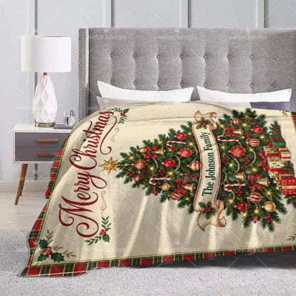 Custom family Christmas blanket displayed on a bed with Merry Christmas text, festive tree ornaments and personalized name.