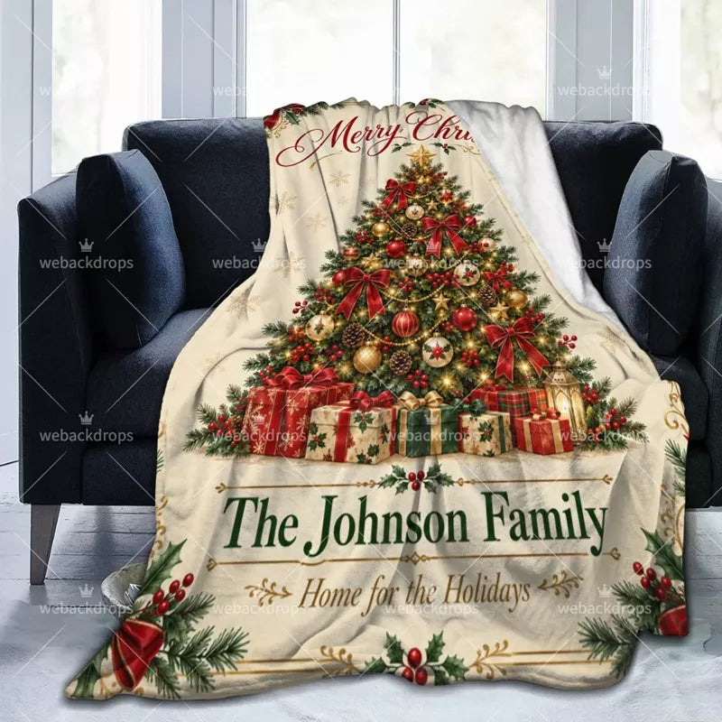 Custom Christmas blanket draped over a dark armchair, featuring red bows, holly, a decorated Christmas tree and personalized family name.