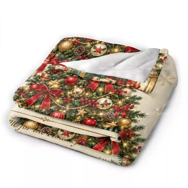 Folded personalized fleece blanket showing festive Christmas ornaments, red ribbon bows, holly berries and soft white backing.