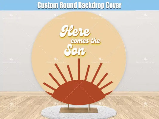 A round backdrop with a retro-inspired 'Here Comes the Son' design featuring a warm sunrise graphic in earthy orange and yellow tones, perfect for baby showers and celebrations.