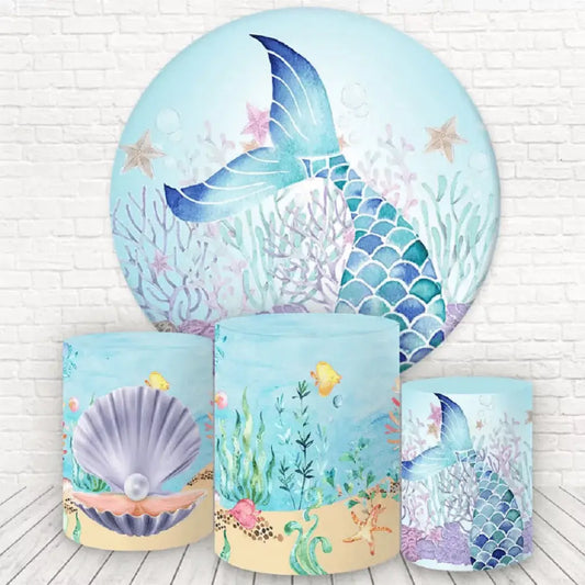 A mermaid-themed party decor set featuring a round backdrop with a shimmering mermaid tail, coral reefs, and sea stars, accompanied by cylinder covers with undersea designs, including a seashell with a pearl, coral reef scenes, and a matching mermaid tail.