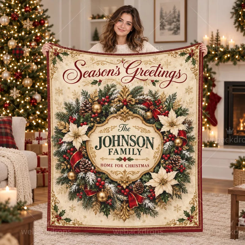 Woman holding a personalized family Christmas blanket with an elegant gold crest, evergreen wreath, and Season's Greetings lettering.