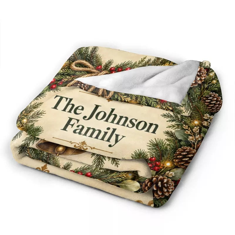 Folded personalized Christmas flannel blanket showing the Johnson family name, printed evergreen branches, pinecones, and soft white backing.