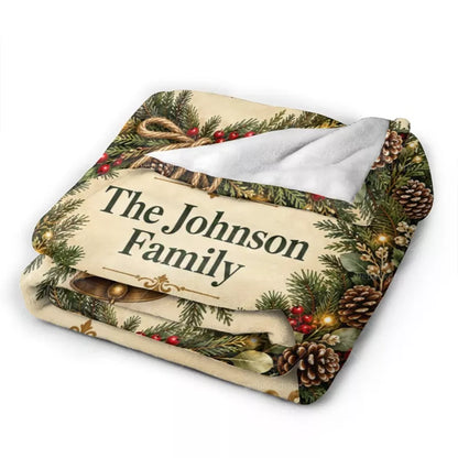 Folded personalized Christmas flannel blanket showing the Johnson family name, printed evergreen branches, pinecones, and soft white backing.