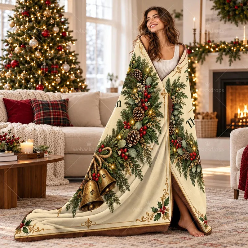 Woman wrapped in a personalized cedar wreath Christmas blanket with vintage bell artwork beside a decorated Christmas tree and fireplace.