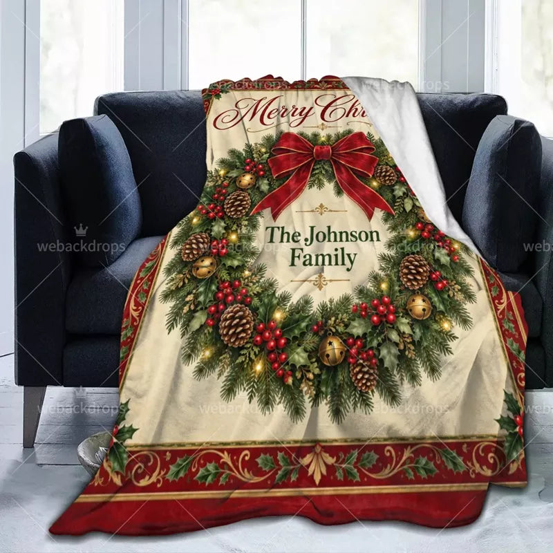 Personalized family Christmas blanket displayed on a dark sofa, showing the vintage wreath print and soft white reverse side.