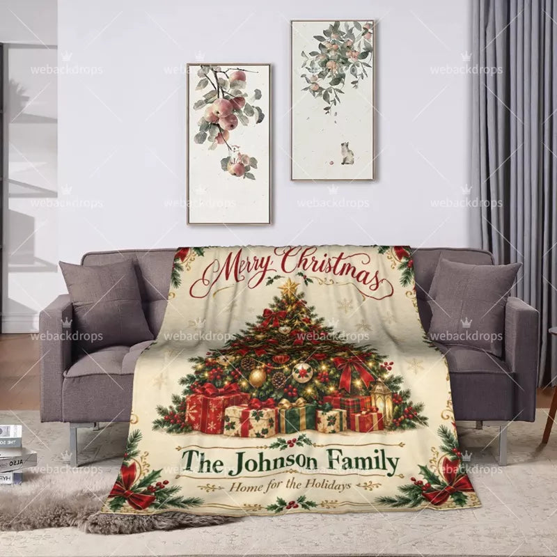 Personalized holly Christmas throw blanket displayed on a gray sofa with festive tree, presents and custom family name.