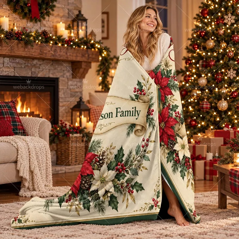 Woman wrapped in a personalized poinsettia Christmas blanket beside a decorated Christmas tree and fireplace in a cozy living room.