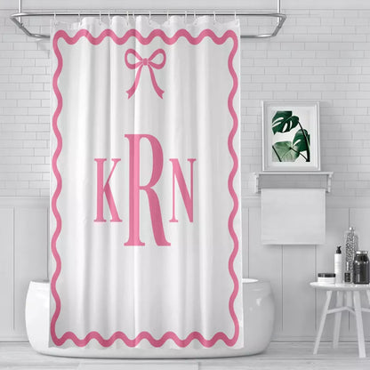 White shower curtain featuring a pink ribbon bow above the KRN monogram, surrounded by a pink wavy border in a tiled bathroom.