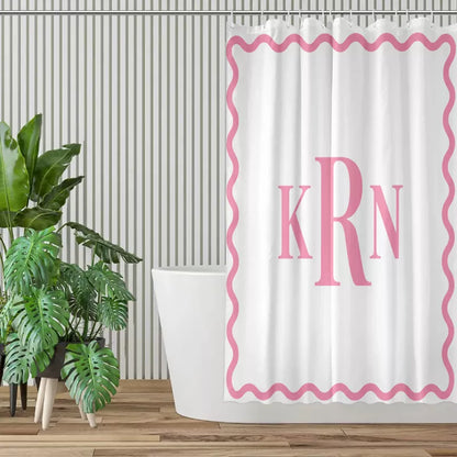 White shower curtain with pink wavy border and KRN initials displayed in a contemporary bathroom with green plants and wooden flooring.