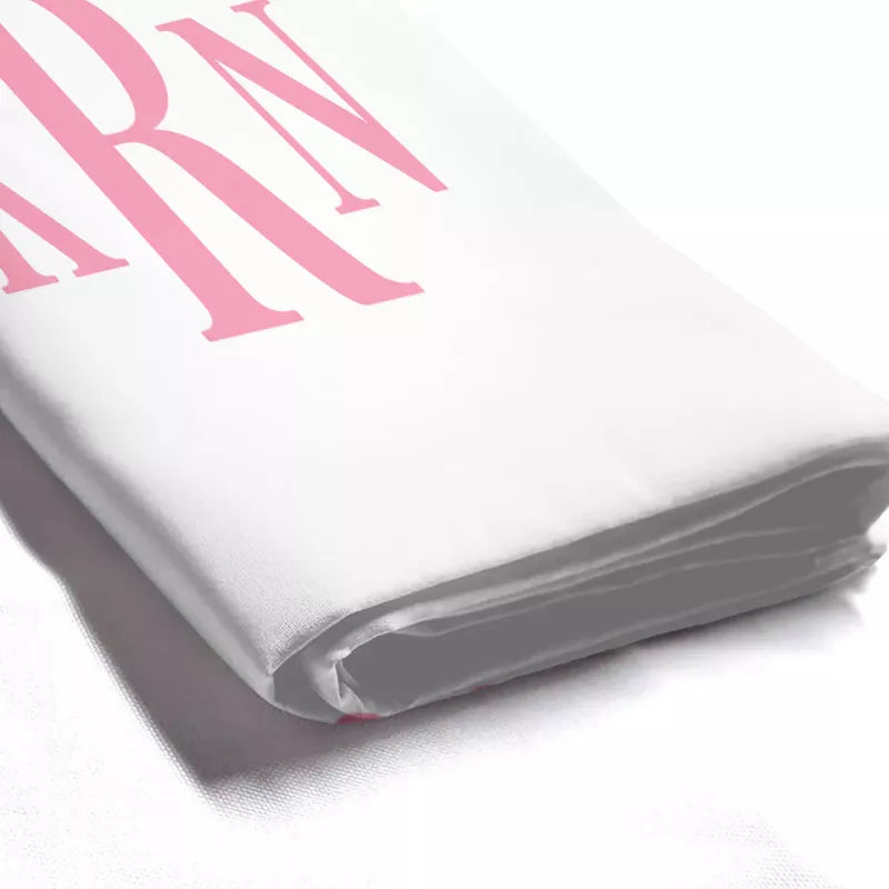 Close-up of folded white shower curtain fabric showing its smooth polyester texture and pink KRN monogram print.