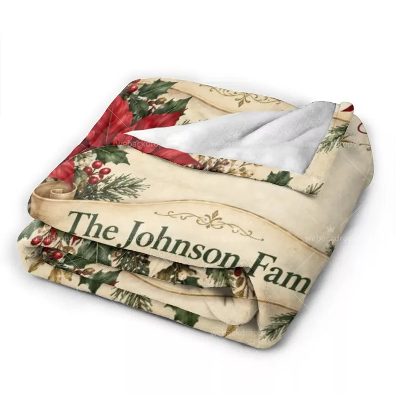 Folded Christmas flannel blanket featuring a personalized family name scroll, red poinsettias, vintage floral details, and white backing.