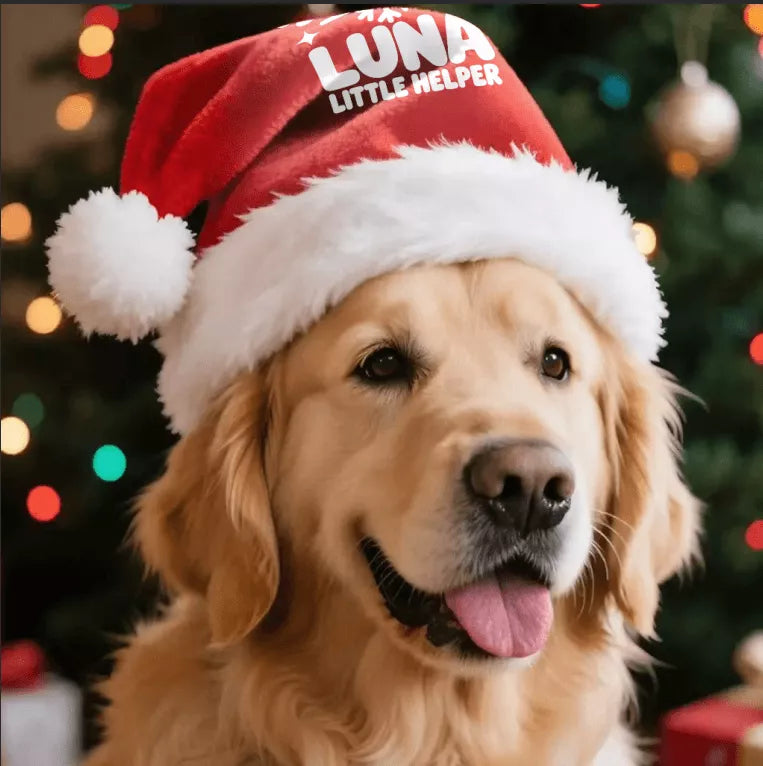 Golden retriever wearing a red Christmas hat with a custom Little Helper design beside a decorated Christmas tree.