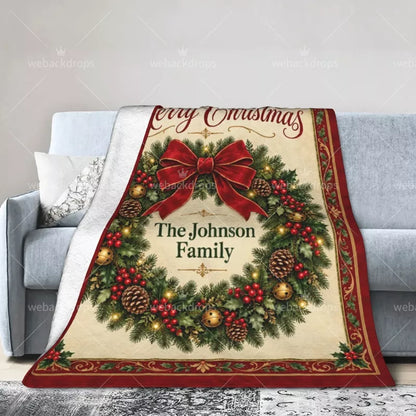 Vintage Christmas wreath blanket draped over a light gray sofa, featuring a red bow, festive greenery, and personalized family name.